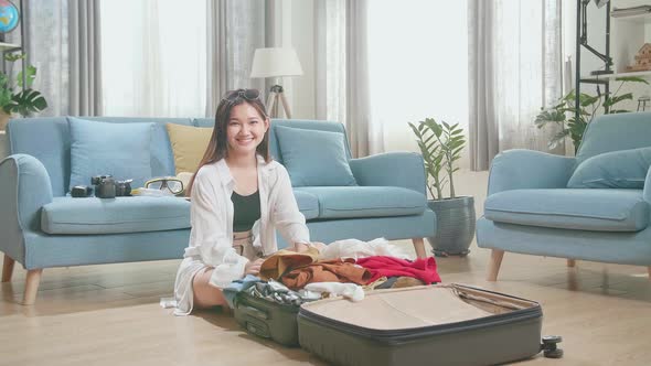 Young Woman Packing Clothes In Suitcase And Warmly Smile To Camera At Home, Preparing For Vacation alt