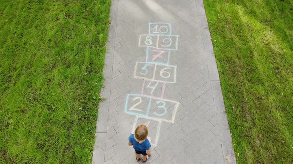 Aerial view of little boy jumping by hopscotch drawn on asphalt