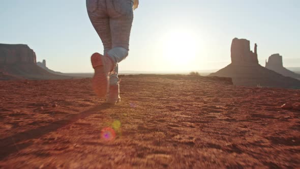 Happy Woman in Pink Traveler Boots Running on Red Mountain Summit at Sunset alt
