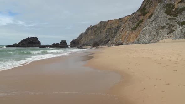Waves Crash on the Sandy Beach near Gruta da Adraga in Portugal