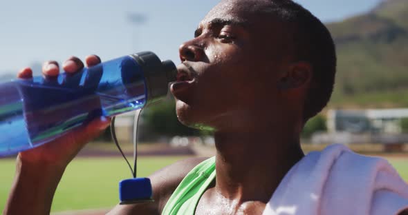 Disabled mixed race man with prosthetic legs sitting on a race track and drinking water alt