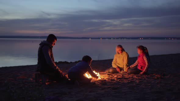 Family of Tourists Resting at Campfire on Night Beach
