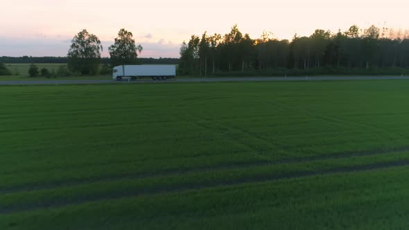 Truck Driving on Road Next to Green Field Aerial View at Sunset alt