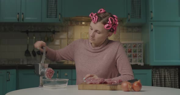30s Young Woman with Hair Curlers on Head Cooking Meat in Mincer Sitting in the Kitchen. Housewife alt