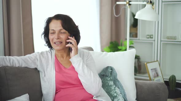 Mature Smiling Woman Talking Phone Sitting on Couch in Home Interior alt