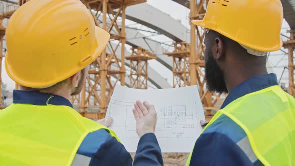 Two Male Construction Workers Discussing Blueprint alt