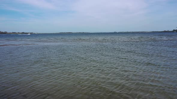 A low angle drone shot over a beach, looking out at the water & the horizon. It is at low tide on a alt