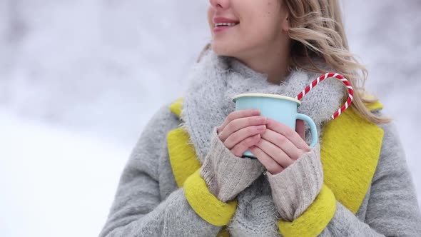 Beautiful woman in coat with cup of hot drink in a snow forest.