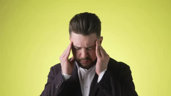 Bearded Young Man in Office Suit Is Putting Hands on Head Having Headache alt