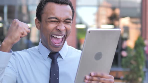 African Businessman Cheering for Success on Tablet Outdoor alt