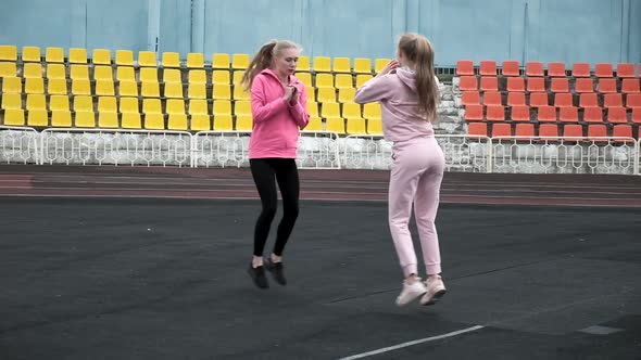 Caucasian Identical Pretty Twins in Sportswear Do Squats and Jumps at Stadium