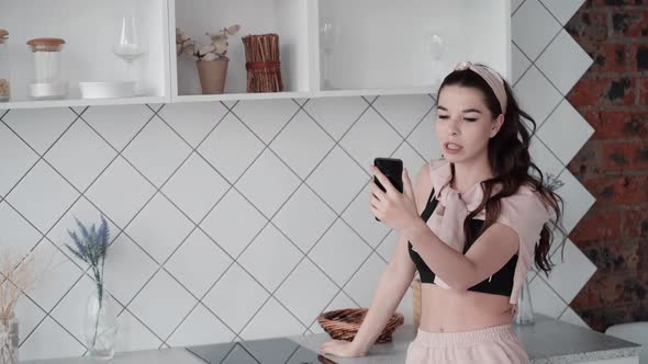 Woman Chatting in Kitchen Using Video Call on Phone. Fashionable Teenager Girl Talking with Friends