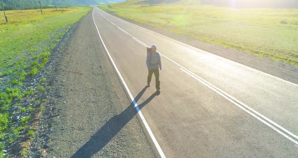 Flight Over Hitchhiker Tourist Walking on Asphalt Road. Huge Rural Valley at Summer Day alt