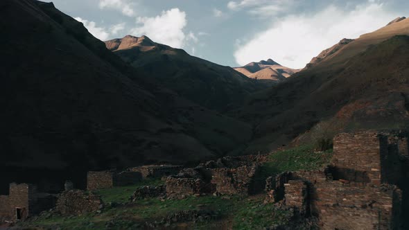 Drone flies over ruins of mysterious hamlet surrounded by caucasus mountains, dusk time in highland