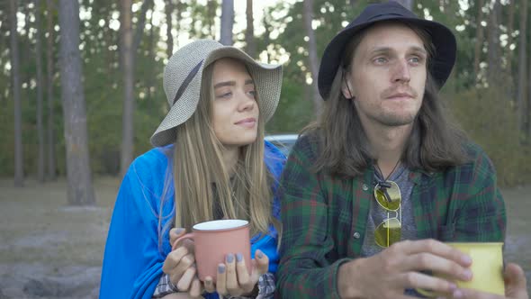 Young Couple of Tourists Sitting in the Forest Drinking Tea or Coffee. Happy Caucasian Man and Woman alt