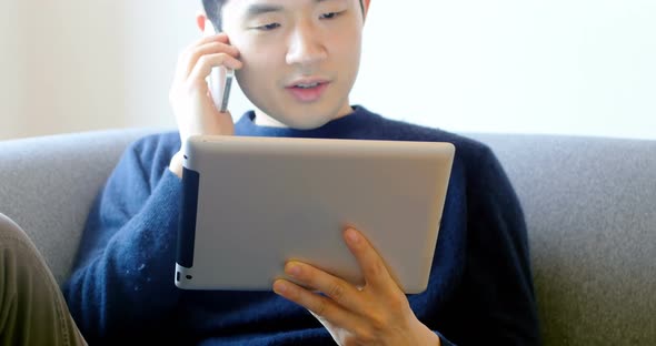 Man talking on mobile phone while using digital tablet in living room 4k alt