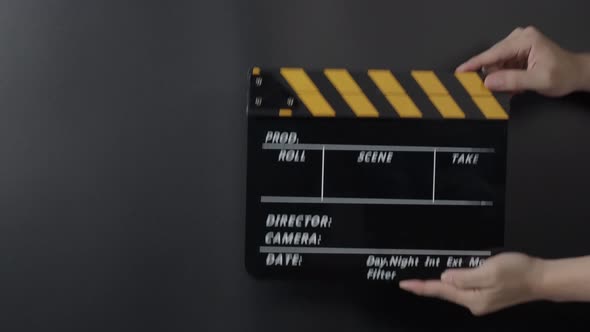 Movie slate or clapperboard hitting. Close up hand holding empty film slate and clapping it on black alt