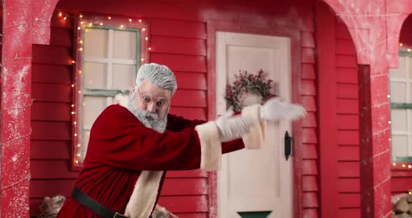 Active Santa Claus Invites Somewhere Making Hand Gestures Against the Background of a Red House with alt