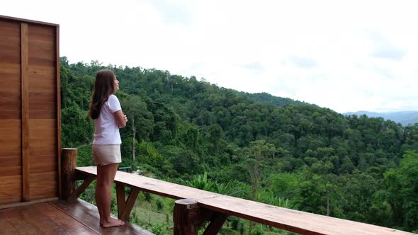 A woman standing on balcony and looking at a beautiful mountains and nature view