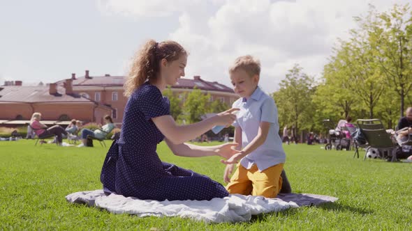 Mother Putting Sunscreen on Little Son in Summer Park alt
