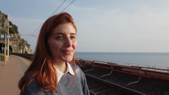 Girl Smiles While Waiting for the Train at the Station Near the Sea alt