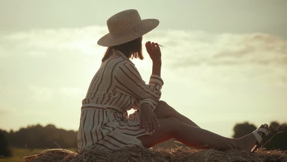 woman in hat resting on a haystack on a sunset background