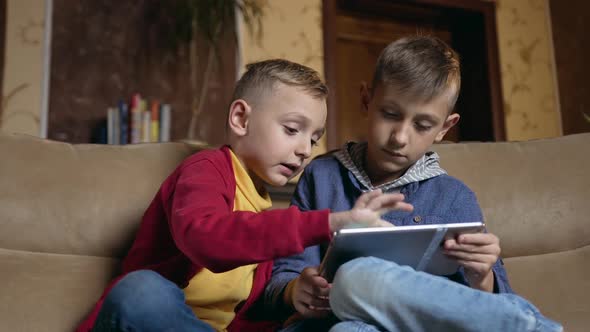 Schoolboys Sitting on Comfortable Sofa in Beautiful Room and Use Tablet PC to Play Online games alt