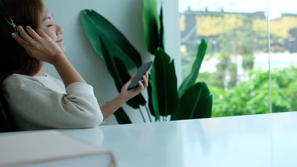 A beautiful young asian woman with headphone enjoy listening to music on smart phone