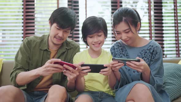 family quality time,asian parent and son sit relax playing game console smartphone at home