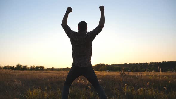 Happy Guy Running Through Grass Field and Victoriously Raising Hands Up at Sunset alt