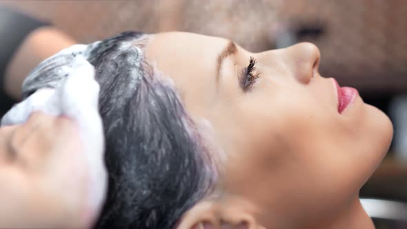 Pleased Female Face During Washing Hairs Using Foam Shampoo By Professional Hairstylist Hands alt