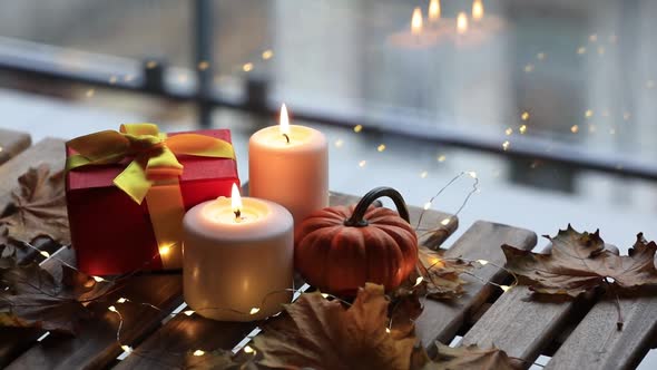 Gift, candles and pumpkin on wooden table with fairy lights