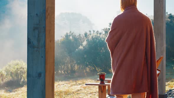 Young Woman Covers Herself with Blanket and Takes Traditional Mate Drink on the Cold Terrace alt