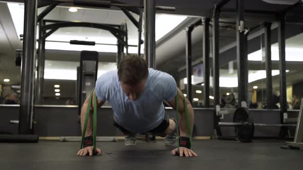 Man doing push-up using a elastic band at the gym. alt