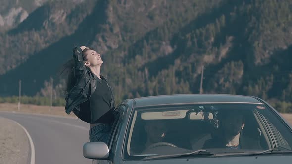 Young Brunette in Black Leather Jacket Sits on Car Window alt