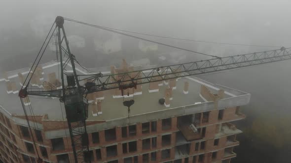 Birds eye view on tower crane in fog standing next to residential building. alt