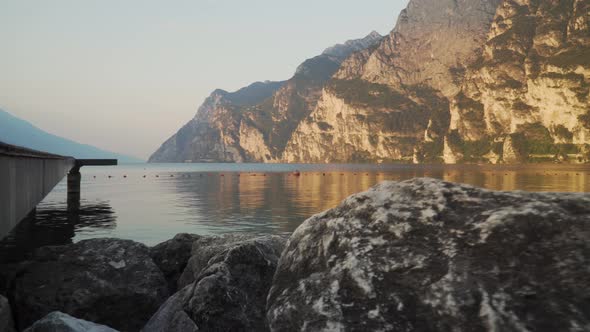 Riva del Garda beach with Garda lake at sunrise. Shooting between rocks in 4k alt