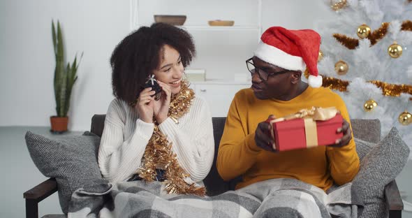 Ethnic Man and Woman Sitting on Sofa Together Exchanging Presents. Afro American Couple Family alt