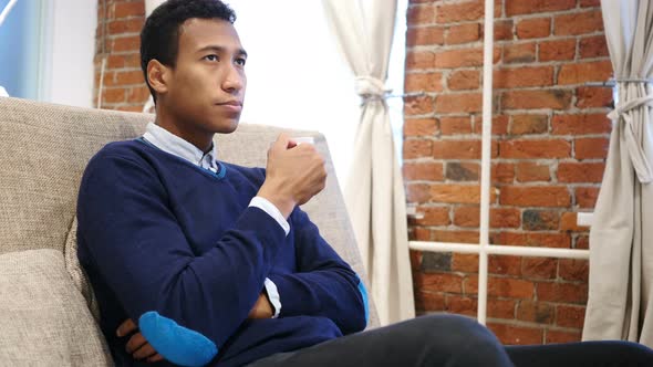 Young African Man Drinking Coffee from Cup Sitting on Sofa alt