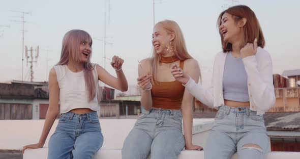 Young Asian women playing sparkle firework with friends. Happy girls celebrating at rooftop party. alt