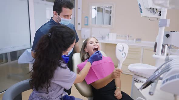 Teenage Girl Opening Mouth Sitting in Dentist Chair As Doctor Consulting MD in Hospital Indoors alt