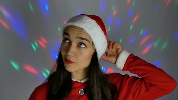 Pretty Young Woman in Santa Claus Hat Smiling and Looking Coquettishly at the Camera. New Year