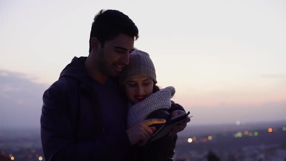 Young Multiethnic Couple Using Tablet Outdoors in Winter After Sunset