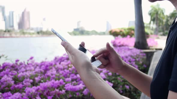 asian young woman sitting at bench in park using smartphone for talking, reading and texting.