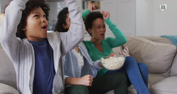 Mixed race lesbian couple and daughter watching tv eating popcorn high fiving alt