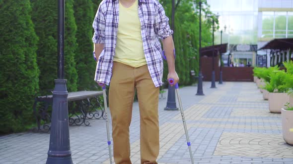 Stylish Man with an Injury on Crutches Walking in the Park on a Sunny Day Slow Mo alt