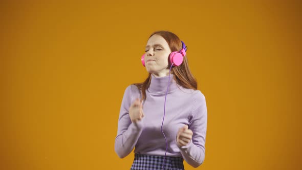 Beautiful Redhaired Young Woman Dances and Sings to Music She Listens to Music with Headphones on an