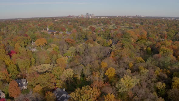 Flyover Autumn trees and houses towards a small church and a park alt