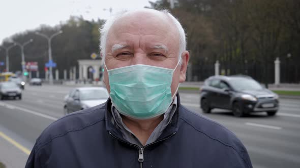 Portrait Of Elderly Man In Virus Proof Mask Standing By Road With Driving Cars alt