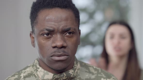 Closeup Portrait of Sad African American Man Looking at Camera As Blurred Furious Caucasian Wife alt